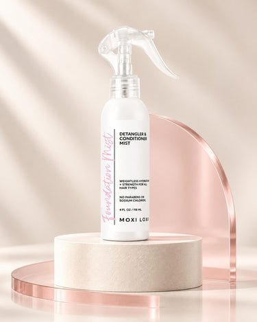 Moxi Loxi Foundation Mist 4 fl oz leave-in detangler and conditioner spray on an ivory studio pedestal