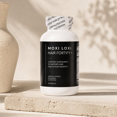 MOXI LOXI Hair Fortify+ daily hair wellness supplement on a warm ivory stone pedestal.