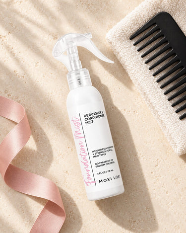 Moxi Loxi Foundation Mist 4 fl oz with an ivory towel and black wide-tooth comb in a salon-care flat lay